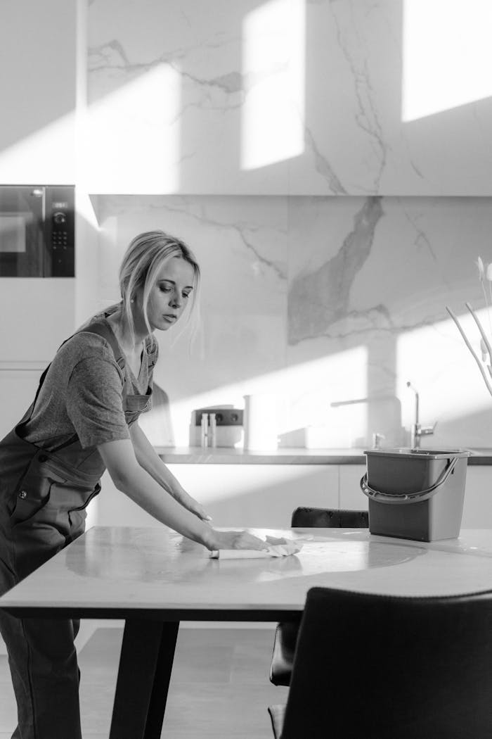 our-story-01 A female cleaner sanitizing a kitchen table with natural light casting shadows.
